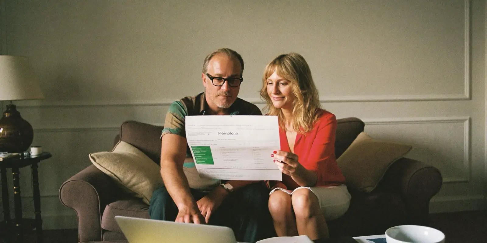 Paar auf dem Sofa bespricht den Pensionskassenausweis am Laptop