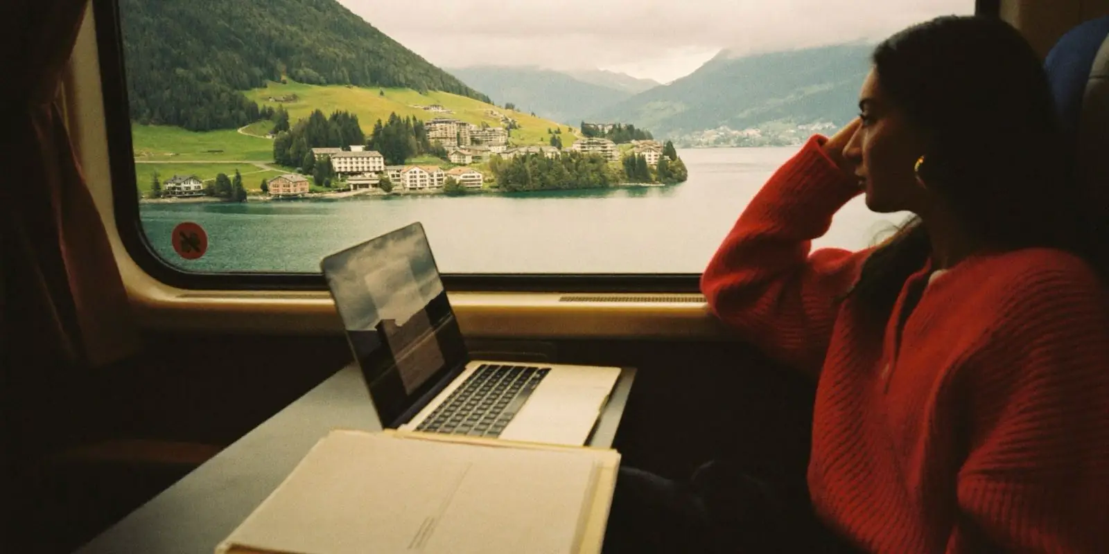 Pendlerin im Zug mit Laptop und Unterlagen, draussen ein Schweizer See